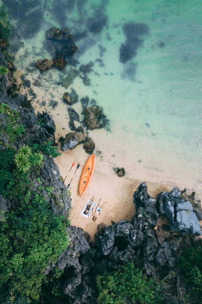 aerial view of sand beach, shallow sea water and rocks with kayak and two people lying down on Cat Ba island Vietnam