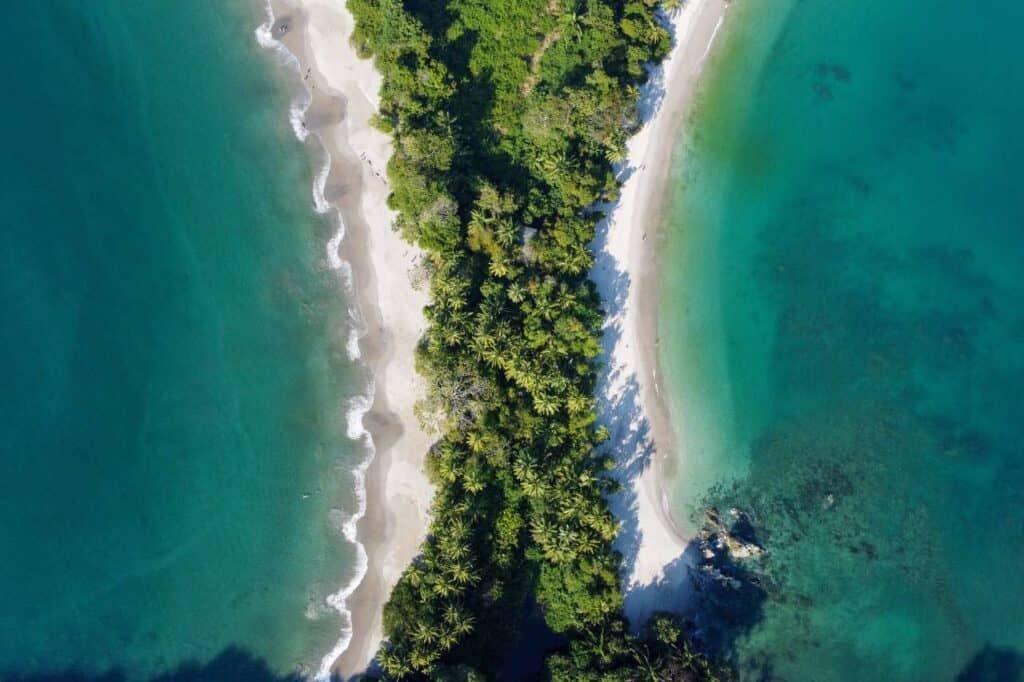 aerial view of green blue pacific ocean with white sand beaches on either side of peninsula at manuel antonio national park costa rica