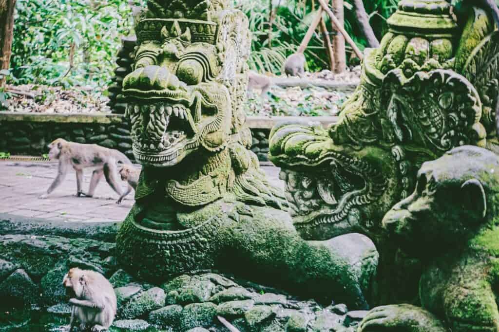 playful monkeys on a stone sculpture in the Sacred Monkey Forest of Ubud, Bali, Indonesia, surrounded by lush green vegetation, one of the most popular things to do in Bali for honeymoon