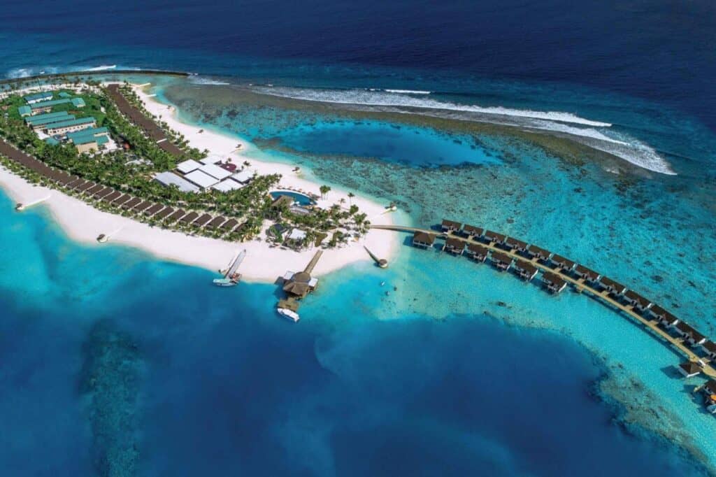 aerial view of white sand island with overwater buildings and palm trees and water slide at oblu select sangeli resort maldives