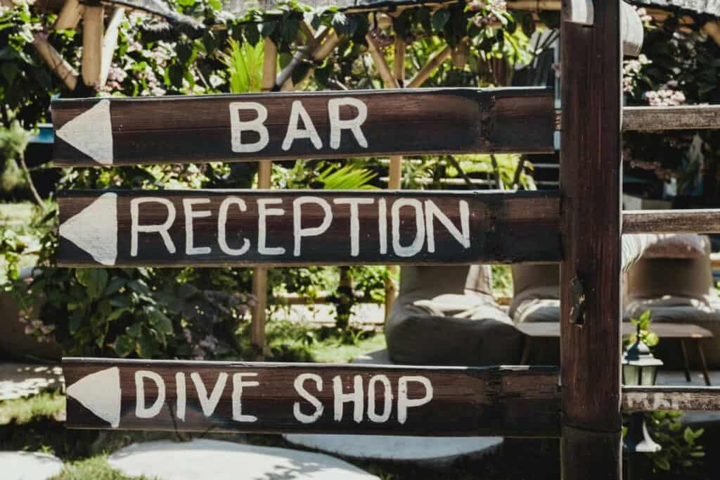 Wooden signpost at a tropical resort in the Gili Island that points to bar reception and scuba diving shop.